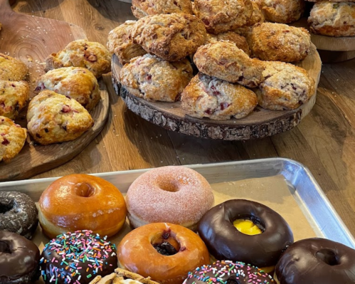 A display of freshly baked scones and assorted donuts on wooden trays and a metal baking sheet.