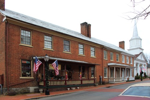 Historic brick buildings line a street, featuring American flags and a church steeple in the background.