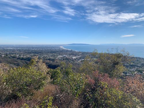 A panoramic view of a coastal city with mountains and ocean under a clear blue sky.