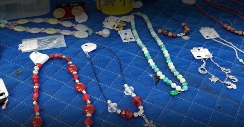 A display of colorful handmade jewelry, including necklaces and earrings, on a blue tablecloth.