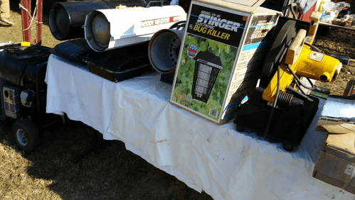 A table displaying various outdoor equipment, including heaters and a bug killer, on a sunny day.