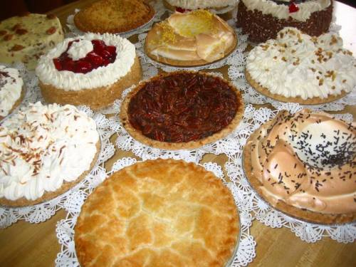 A variety of delicious cakes and pies displayed on a wooden table, featuring different toppings and crusts.