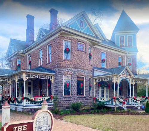 A historic brick house decorated with holiday wreaths, featuring porches and a tall turret.