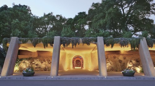 A modern architectural entrance with stone columns, soft lighting, and greenery, set against a natural backdrop.