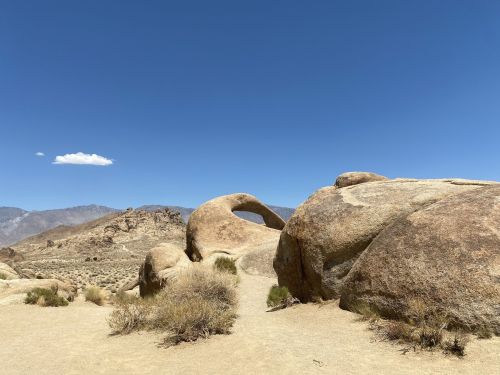 A rocky landscape featuring large boulders and a natural arch under a clear blue sky.