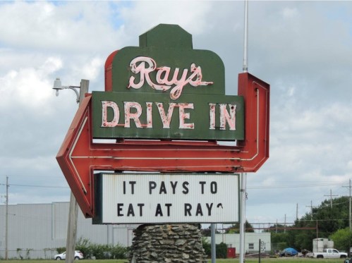 Sign for Ray's Drive-In featuring a large arrow and the message "It pays to eat at Ray's." Cloudy sky in the background.