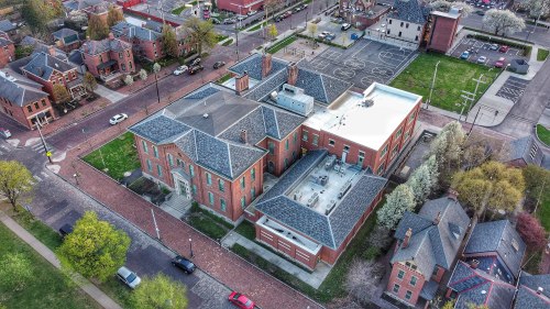 Aerial view of a large brick building surrounded by green spaces and residential areas, with playgrounds nearby.