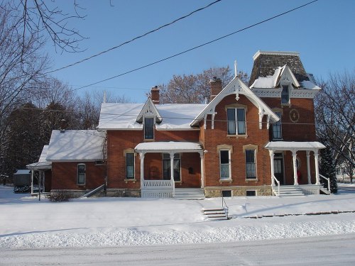 A large brick house with a steep roof, surrounded by snow, under a clear blue sky.