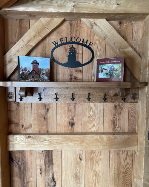A wooden door with a "Welcome" sign, featuring a shelf with two framed pictures and several hooks below.