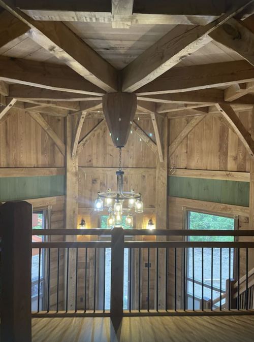 Interior view of a wooden cabin with a high ceiling, featuring a chandelier and a decorative mounted deer head.
