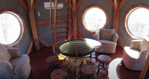 Cozy interior of a treehouse with circular windows, wooden furniture, and a central table made from a tree stump.