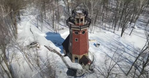 Aerial view of a tall, red and white tower surrounded by snow-covered trees in a winter landscape.
