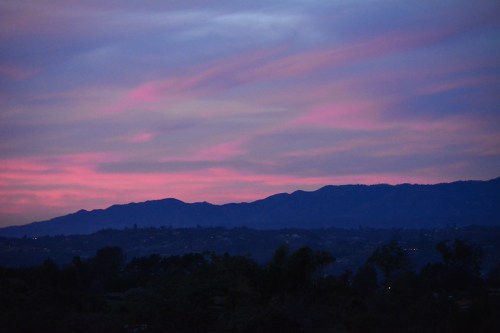 A serene twilight sky with pink and purple hues above dark mountain silhouettes.