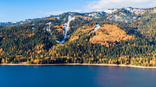 A serene lake surrounded by vibrant autumn foliage and snow-capped mountains under a clear blue sky.
