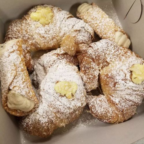 A box filled with powdered sugar-dusted pastries, including croissants and cream-filled cannoli.