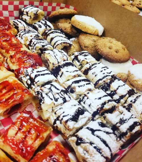 A variety of pastries and cookies arranged in a box, featuring drizzled chocolate and fruit toppings.