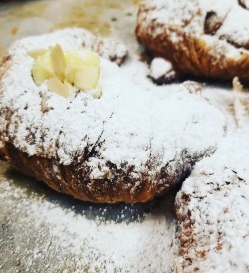 Close-up of a flaky pastry dusted with powdered sugar and topped with a slice of almond.