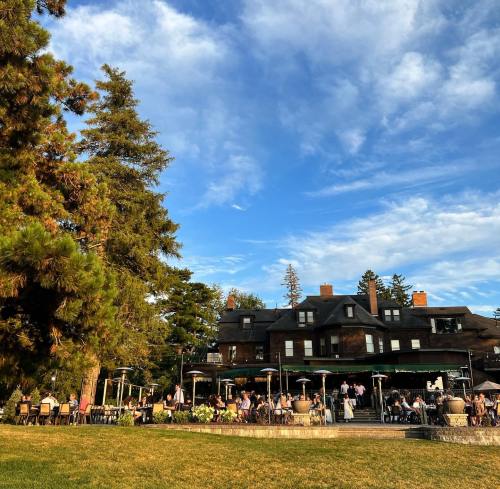 A historic building with a patio, surrounded by trees, filled with people enjoying a sunny day outdoors.