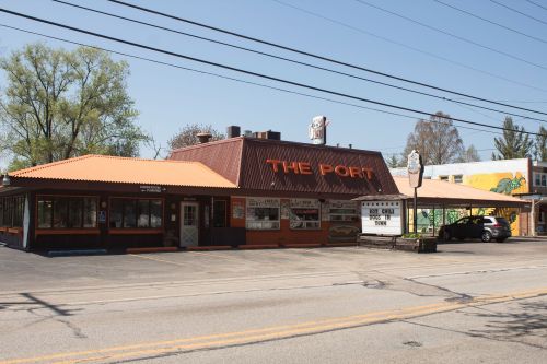 A restaurant named "The Port" with an orange roof, surrounded by trees and parked cars on a sunny day.