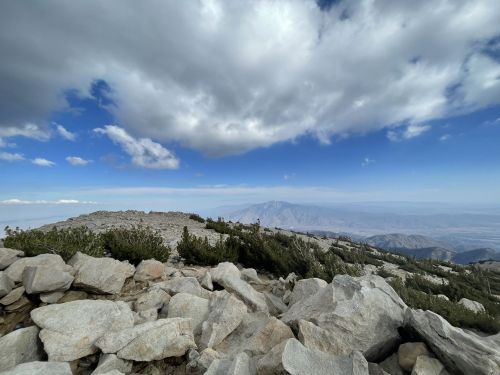 A rocky mountain landscape under a partly cloudy sky, with distant mountains visible in the background.
