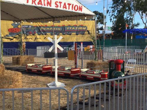 A small train station with a colorful train, hay bales, and a crossing sign under a tent.