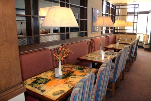 Cozy restaurant interior with striped chairs, tables adorned with vintage decor, and soft lighting from hanging lamps.