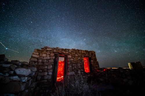 A starry night sky above the ruins of a stone building, with glowing red light illuminating the interior.