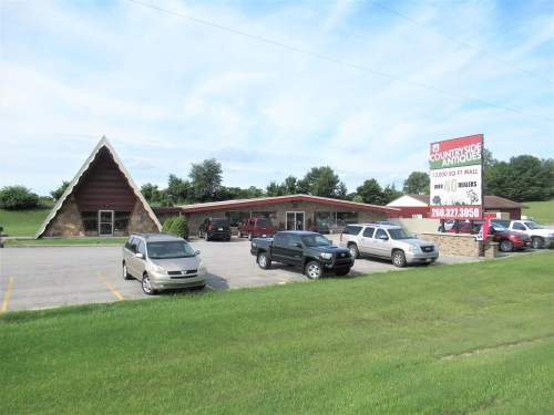 A triangular-roofed building with a sign, surrounded by parked cars and green grass under a blue sky.