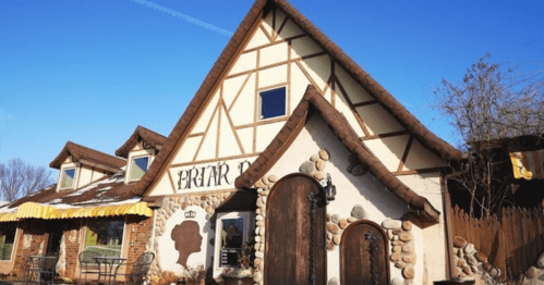 A whimsical building with a steep, gabled roof, stone accents, and a sign reading "Priar." Clear blue sky above.