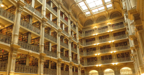 A grand library interior with multiple levels of bookshelves and ornate architecture, illuminated by natural light.