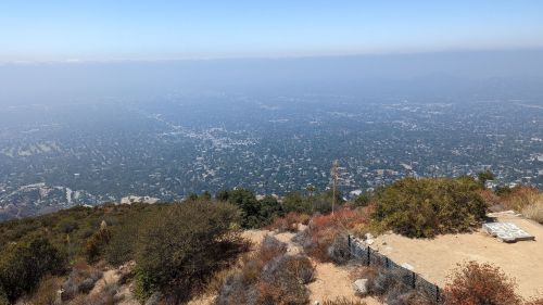 A panoramic view from a mountain overlooking a hazy cityscape and surrounding greenery.