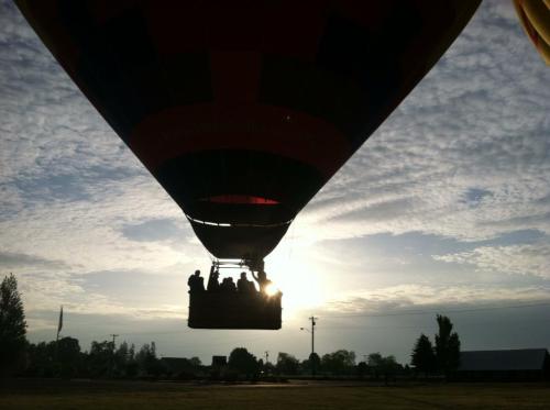 Silhouette of a hot air balloon with passengers against a sunrise and cloudy sky.