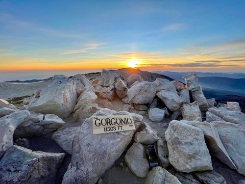 Sunset view from Gorgonio Mountain summit, with a sign marking the elevation at 11,503 feet among rocky terrain.