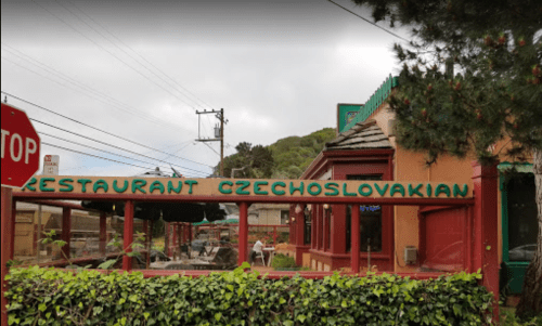 Exterior of Restaurant Czechoslovakian, featuring a colorful sign and outdoor seating under a cloudy sky.