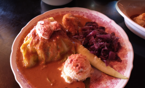 A plate of stuffed cabbage with a creamy sauce, accompanied by red cabbage and a scoop of rice.