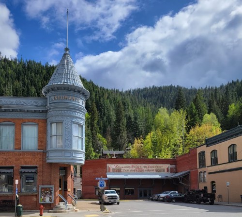 Historic building with a turret, surrounded by trees and mountains under a partly cloudy sky.