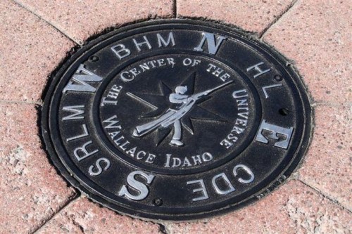 A metal plaque on the ground marking the "Center of the Universe" in Idaho, featuring directional indicators.