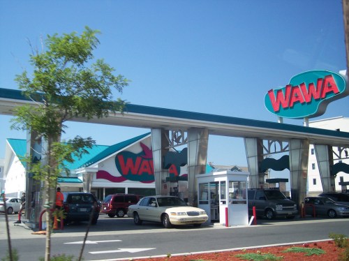 A Wawa gas station with multiple cars parked and a clear blue sky in the background.