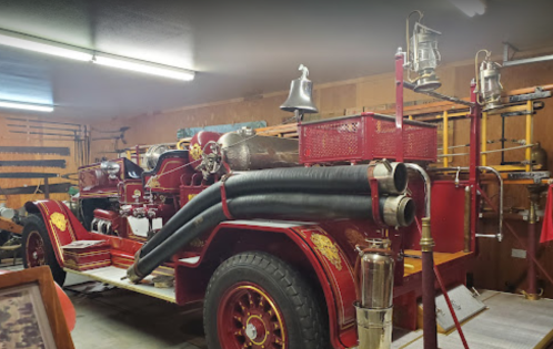 A vintage fire truck displayed in a garage, featuring red paint, hoses, and antique firefighting equipment.