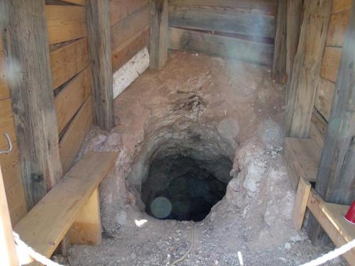 A wooden structure with benches surrounding a deep, circular hole in the ground, suggesting a mining or excavation site.