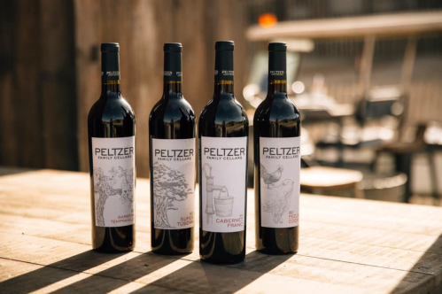 Four bottles of Peltzer Family Cellars wine displayed on a wooden table, featuring unique labels and a rustic background.
