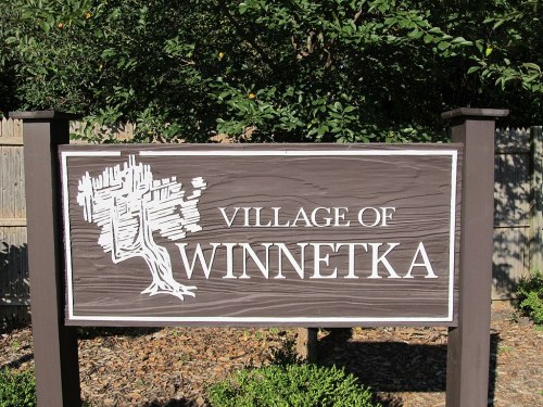 Sign for the Village of Winnetka, featuring a tree graphic and surrounded by greenery.