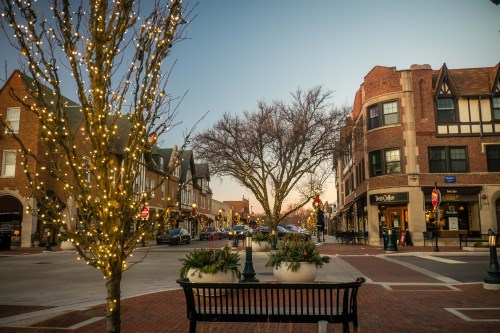 A quiet street at dusk, lined with shops and trees adorned with lights, creating a festive atmosphere.