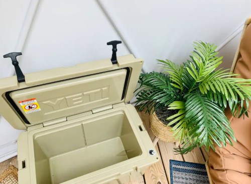 A YETI cooler with the lid open, next to a potted plant, on a wooden floor.