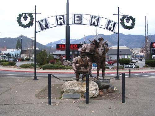 A bronze statue of a cowboy and a donkey under a sign reading "YREKA," decorated with wreaths.