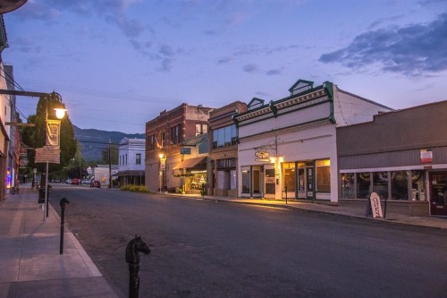Quiet street scene at dusk, featuring historic buildings and soft streetlights illuminating the empty road.
