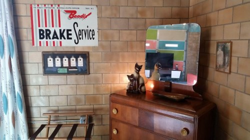 A vintage room corner featuring a mirror, a wooden dresser, decorative cats, and a retro sign for brake service.