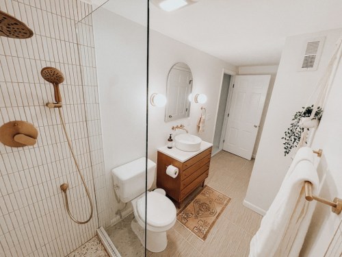 Modern bathroom featuring a glass shower, wooden vanity, and neutral decor with a touch of greenery.