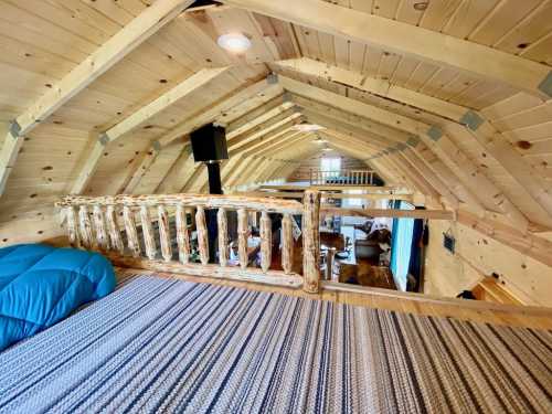 Cozy loft space with wooden beams, a railing, and a view of a rustic living area below.