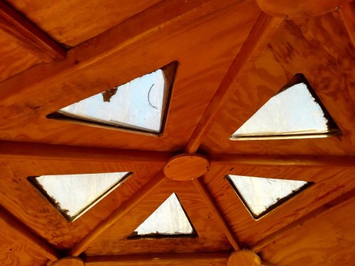View of a wooden ceiling with triangular skylights, showcasing a geometric design and natural light filtering through.